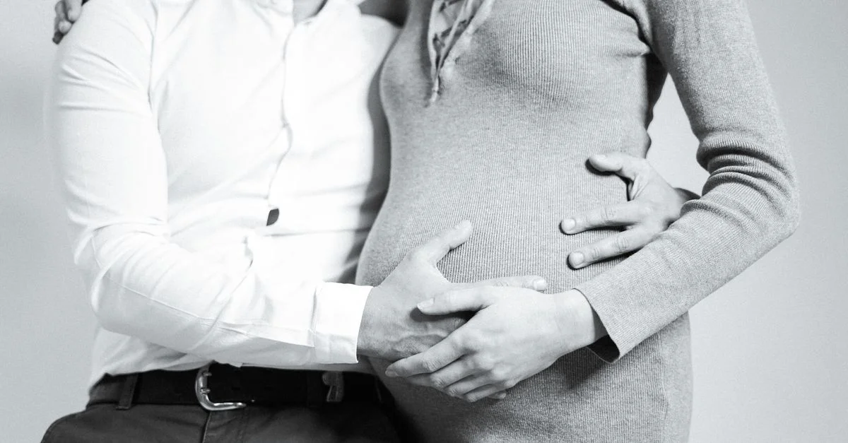 Un couple s'embrassant tendrement avec les mains sur un ventre enceinte, symbolisant la famille et l'amour.