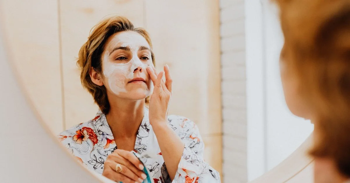Une femme appliquant un masque cosmétique pour le soin de la peau devant un miroir.