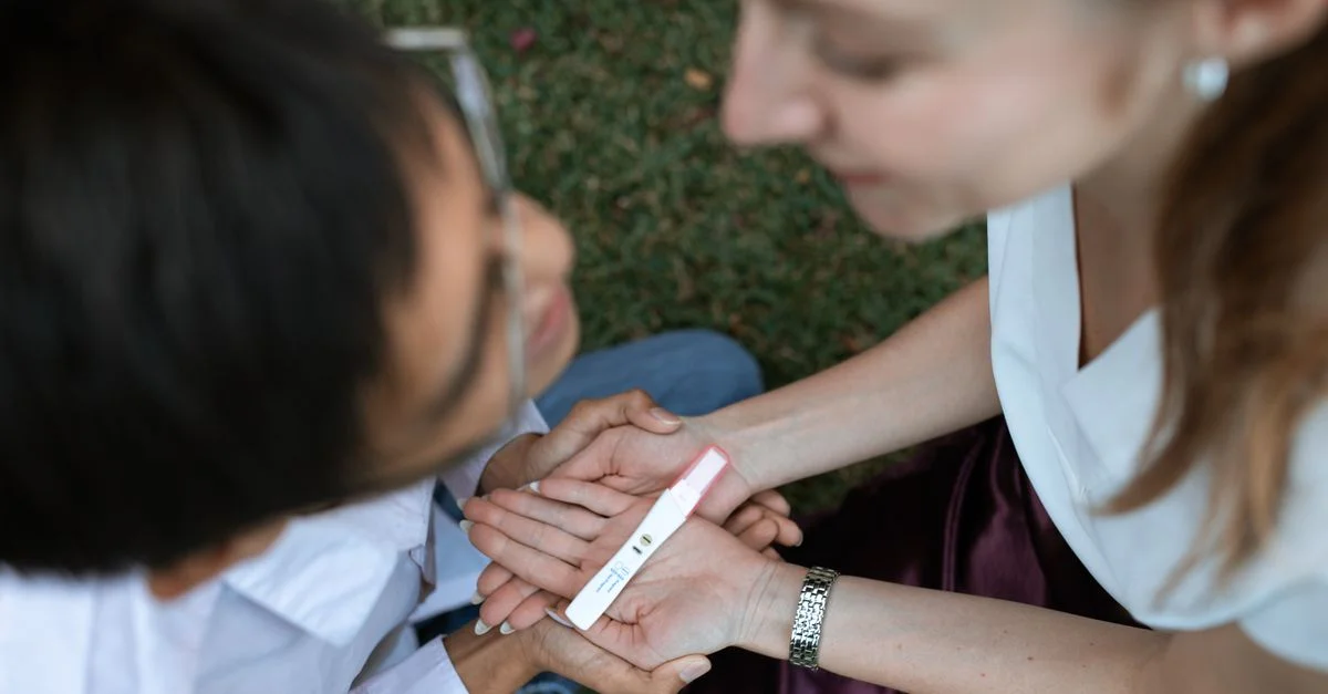 Un couple heureux réagit avec joie à un résultat positif d'un test de grossesse dans un cadre extérieur paisible.