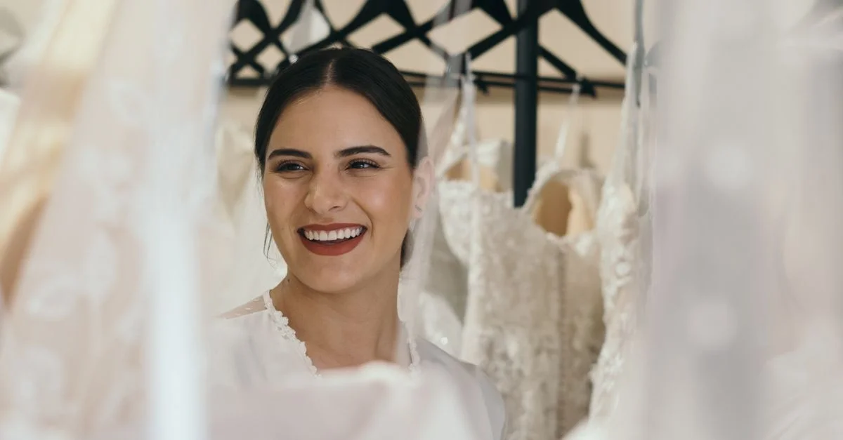 Une mariée joyeuse sourit entourée de belles robes de mariée sur des cintres.