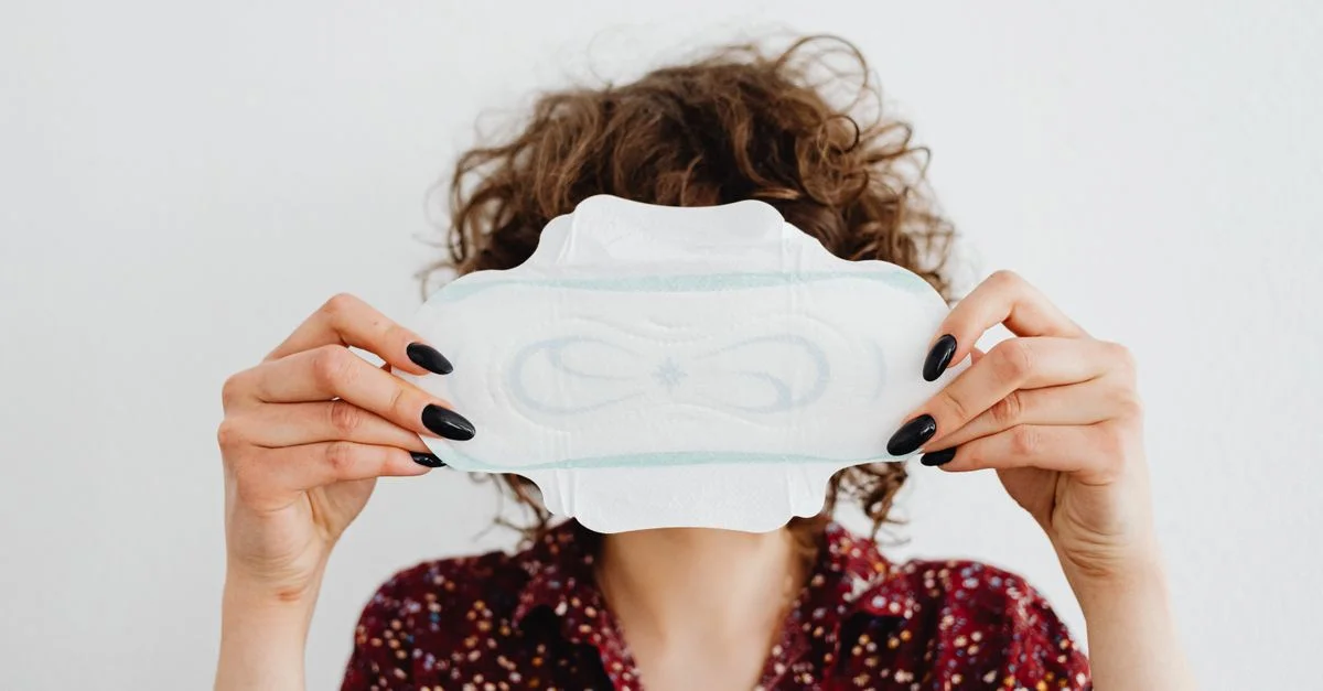 Une femme tenant une serviette hygiénique, mettant en avant les questions de santé menstruelle et d'hygiène.