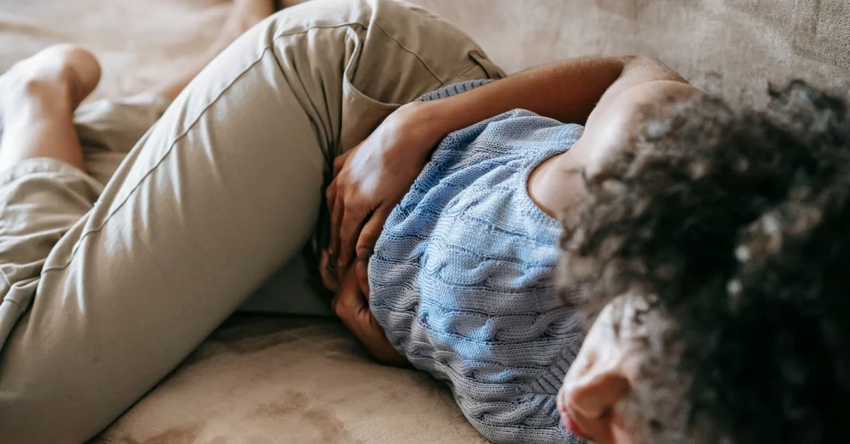 Une femme allongée sur un canapé, tenant son ventre, ressentant de l'inconfort et de la douleur.