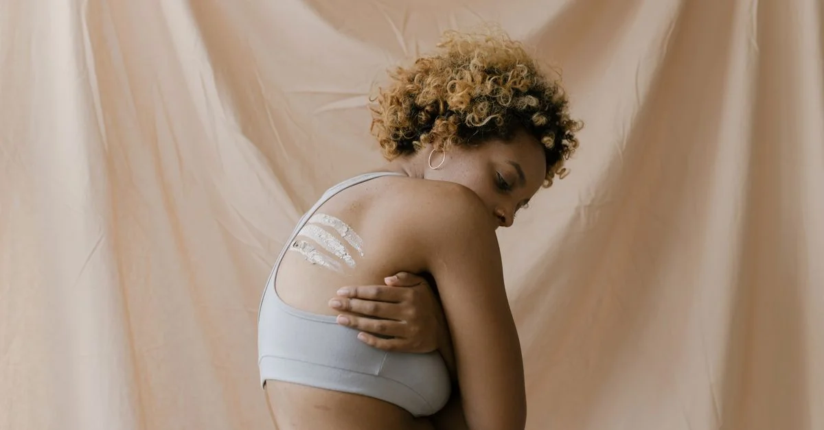 Femme afro-américaine appliquant de la crème pour la peau sur son dos avec un arrière-plan naturel.
