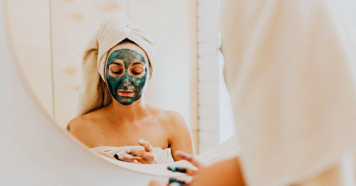 Une femme profite d'une routine de soins apaisante avec un masque facial, se reflétant dans le miroir.