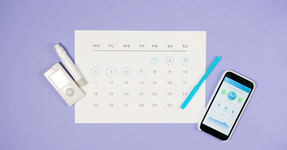 Vue de dessus d'un calendrier avec des dispositifs médicaux et un smartphone, représentant la gestion du diabète.