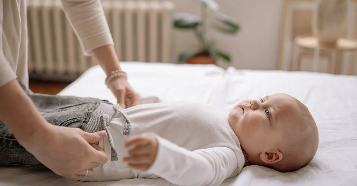 Une mère habille tendrement son bébé sur un lit, mettant en valeur un moment de parentalité doux à l'intérieur.