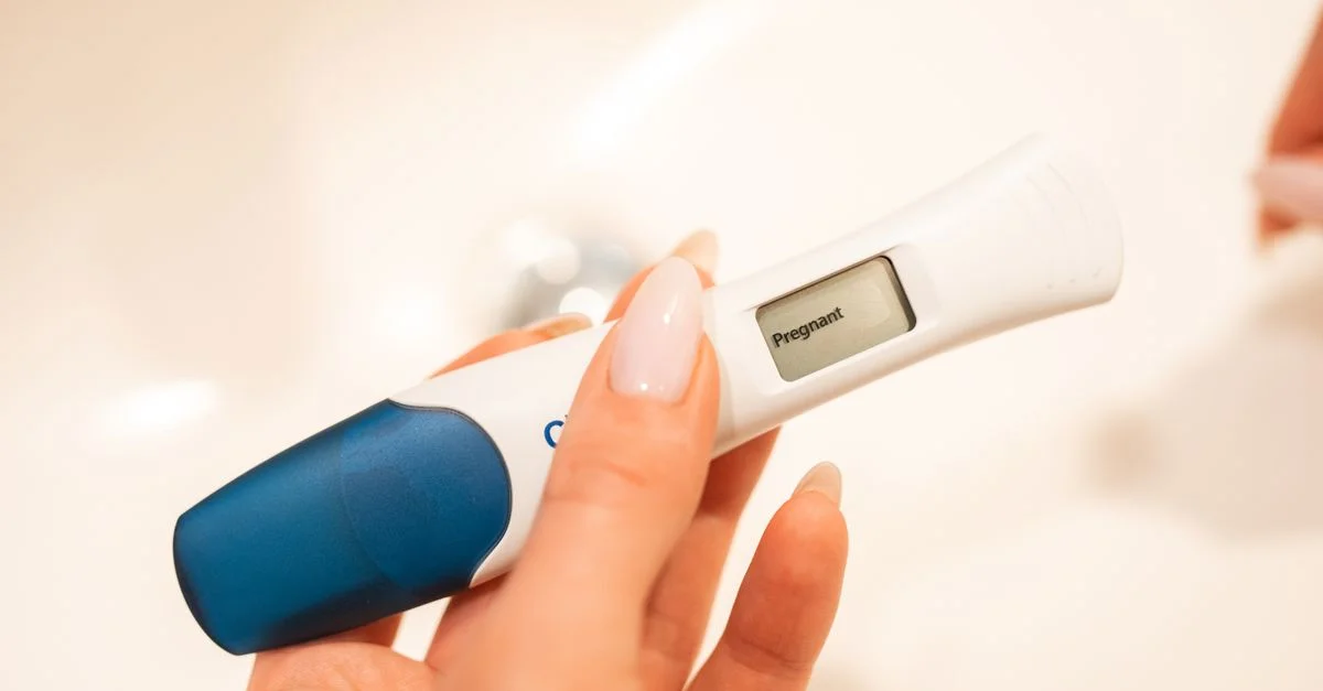 Vue rapprochée d'un test de grossesse numérique positif tenu par une femme avec des ongles manucurés.