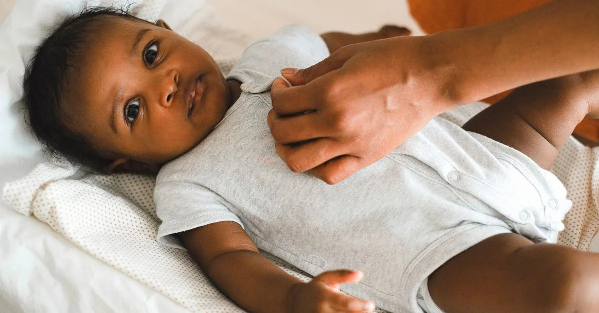 Gros plan d'une mère habillant son bébé dans une légère combinaison à l'intérieur.