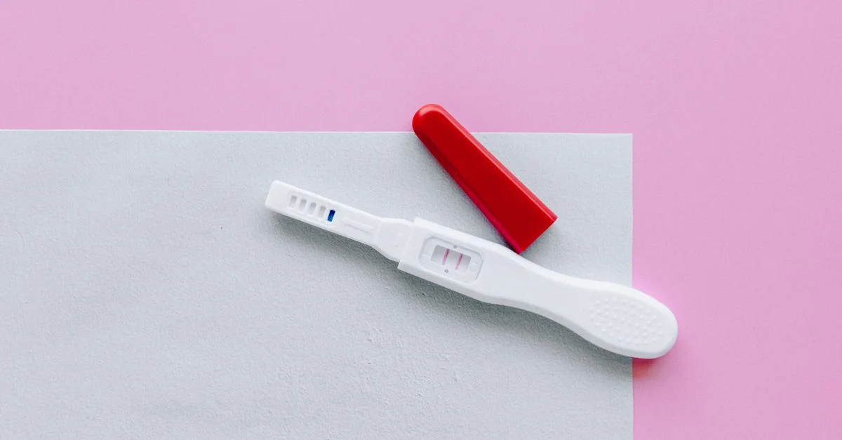 Un test de grossesse positif avec un capuchon rouge sur une surface rose et blanche en style flat lay.